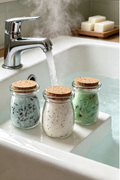 3 glass jars with cork stoppers sitting on the edge of a white bath with hot steamy water coming out of a steel tap