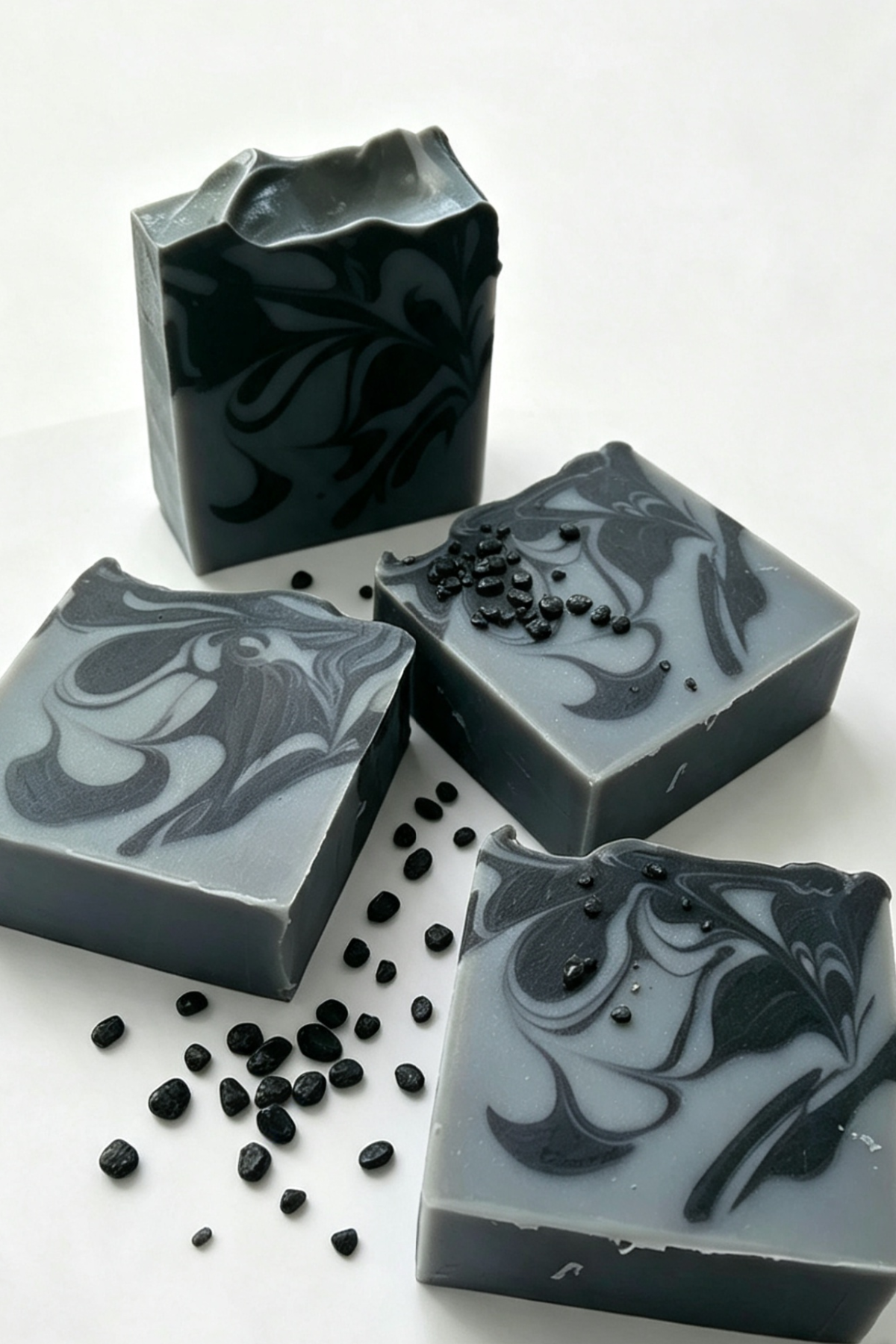 4 soaps with a textured top, black & bluey grey swirl design, surround by charcoal pips