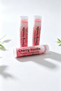 3 lip balm sticks on a white background surrounded by sprigs of green leaves