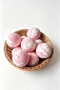 Pink and white marbled bath bombs arranged in a small woven wicker basket on a clean white background.