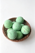 A group of round mint green bath bombs with small red speckles, arranged in a brown woven wicker basket on a clean white background.